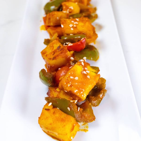 Sattvik Foods' Indian paneer dish with bell peppers and sesame seeds on a white plate.