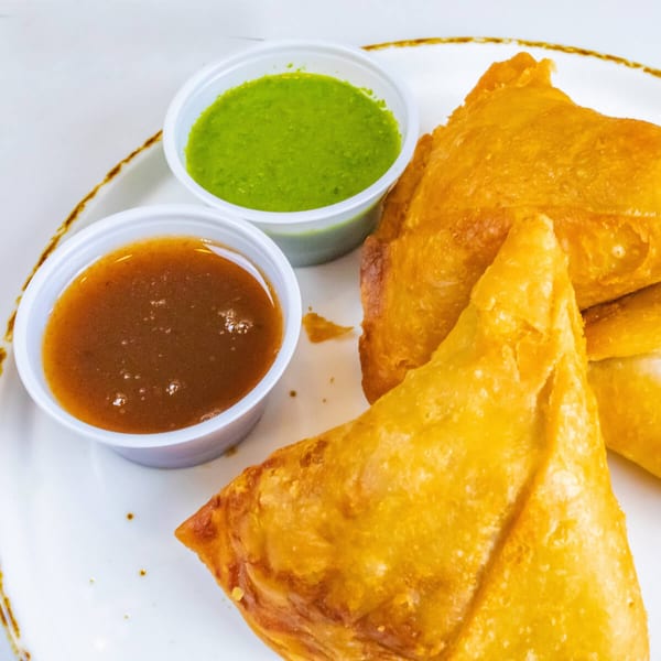 Golden-fried Indian samosas with green chutney and tamarind sauce on a white plate.