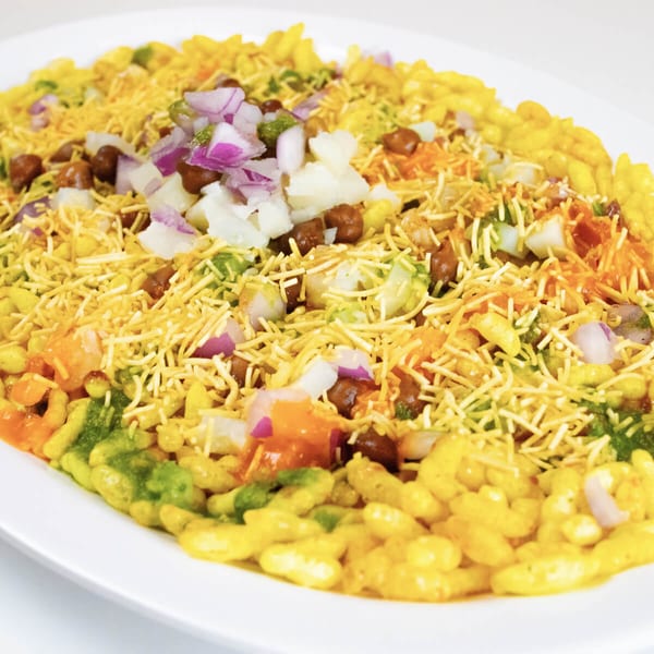 A vibrant Indian Bhel Puri dish, topped with sev, chopped onions, potatoes, and chickpeas.